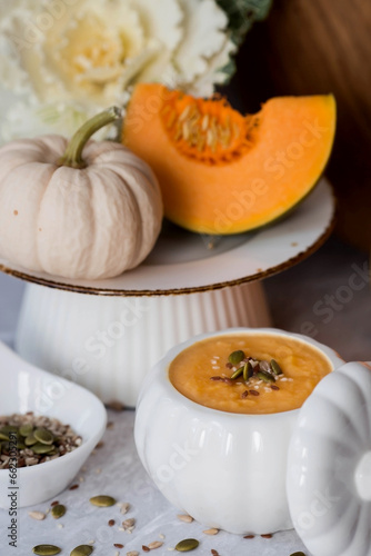 Seasonal autumn food. Traditional pumpkin cream soup in a pumpkin-shaped bowl and fresh pumpkin on a gray marble background.