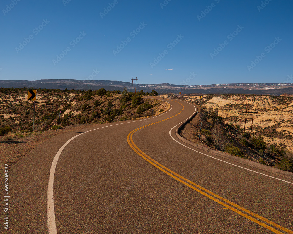 Winding road in a desertic landscape in Utah, USA. Clear blue sky and empty road.