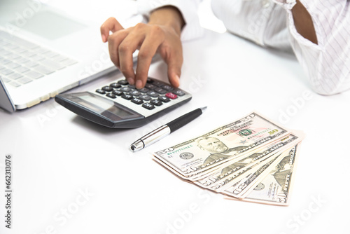 Close-up of woman's hand using calculator and stacks of dollar bills