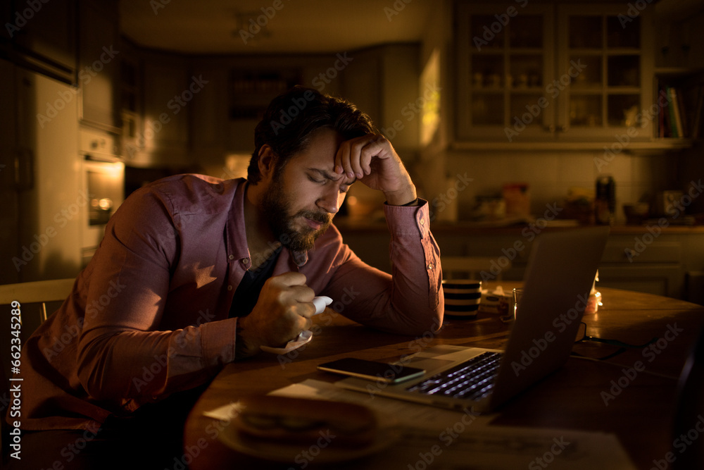 Stressed young man doing financials in the kitchen at night Stressed young man doing financials in the kitchen at night
