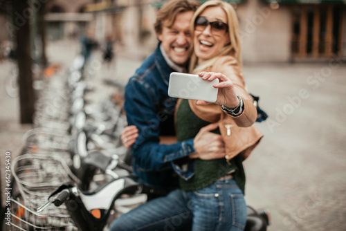 Middle aged Caucasian couple taking a selfie on a smartphone at the bike sharing program in the city © Geber86