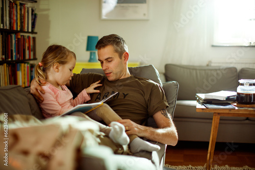 Young father reading with his daughter on the couch after coming back from the army at home