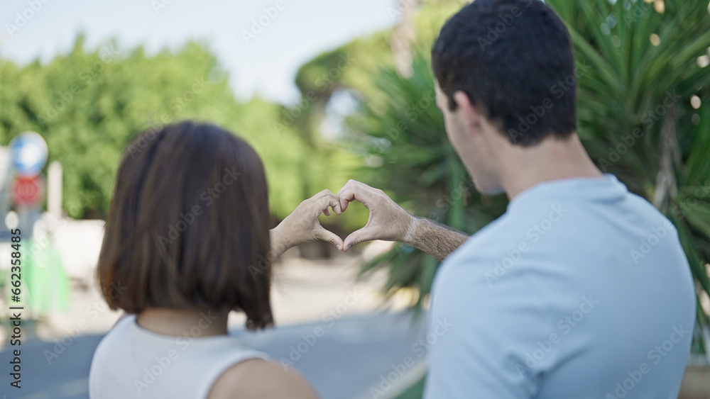 Beautiful couple doing heart gesture with hands standing backwards at park Beautiful couple doing heart gesture with hands standing backwards at park