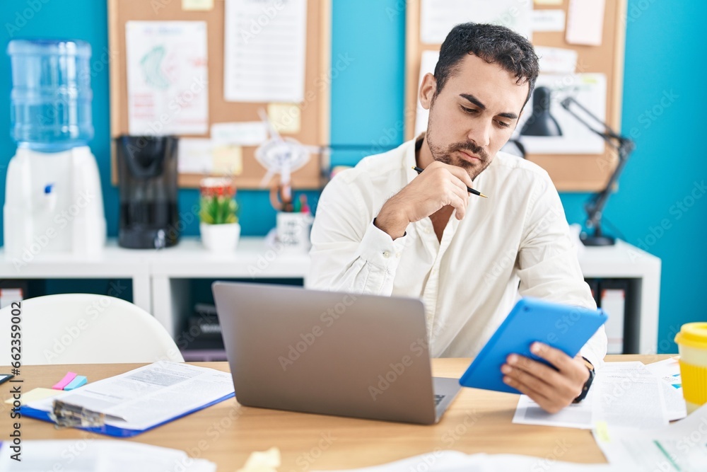Young hispanic man business worker using touchpad and laptop at office Young hispanic man business worker using touchpad and laptop at office