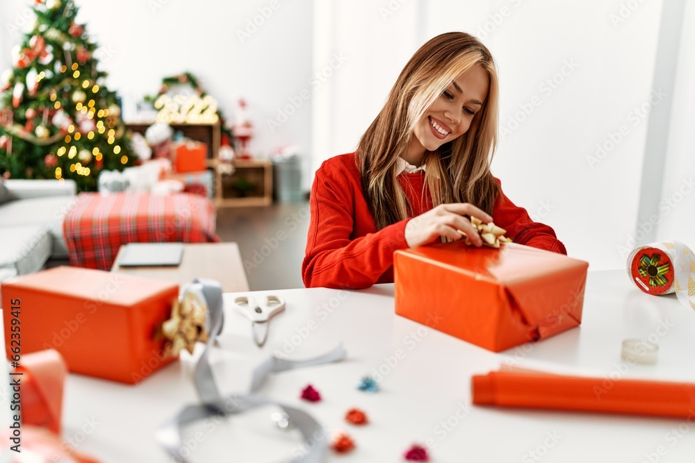 Young caucasian woman preparing gift sitting by christmas tree at home Young caucasian woman preparing gift sitting by christmas tree at home