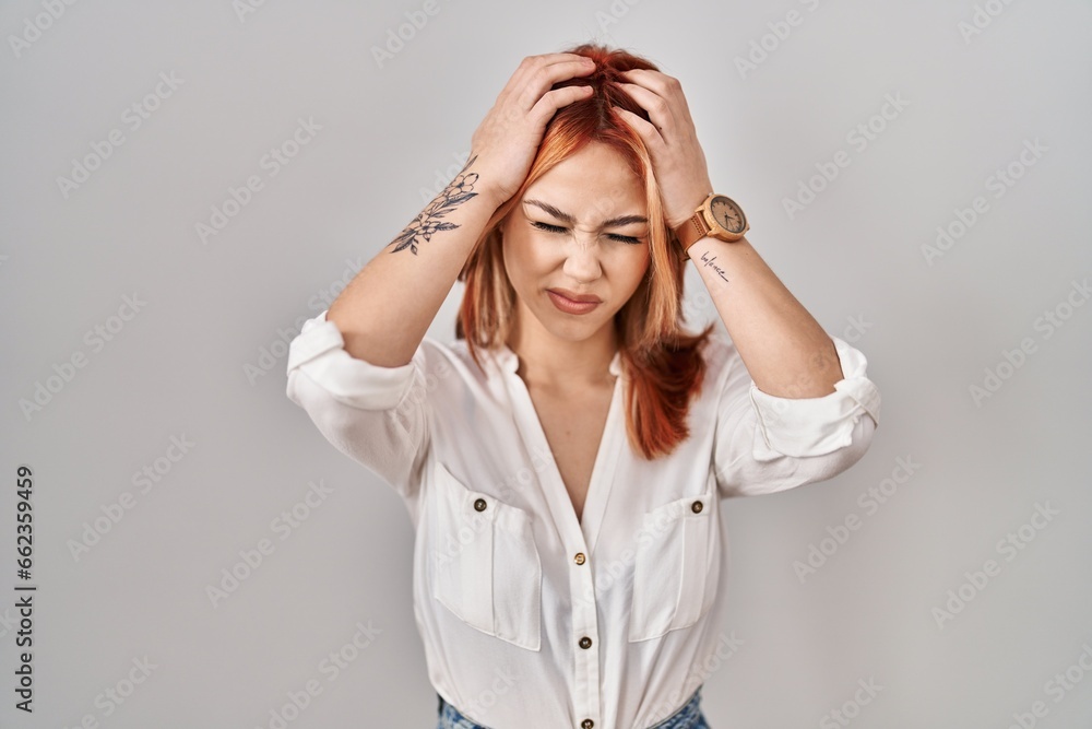 Young caucasian woman standing over isolated background suffering from headache desperate and stressed because pain and migraine. hands on head. Young caucasian woman standing over isolated background suffering from headache desperate and stressed because pain and migraine. hands on head.