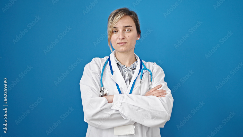 Young blonde woman doctor standing with arms crossed gesture over isolated blue background Young blonde woman doctor standing with arms crossed gesture over isolated blue background