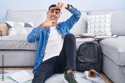 Young hispanic man sitting on the floor studying for university smiling making frame with hands and fingers with happy face. creativity and photography concept.