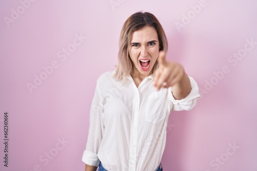 Young beautiful woman standing over pink background pointing displeased and frustrated to the camera, angry and furious with you