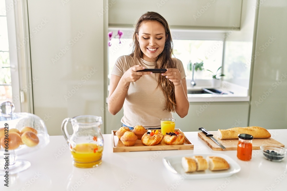 Young beautiful hispanic woman make photo by smartphone to breakfast at the kitchen Young beautiful hispanic woman make photo by smartphone to breakfast at the kitchen