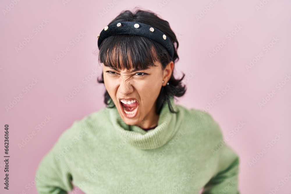 Young beautiful woman standing over pink background angry and mad screaming frustrated and furious, shouting with anger. rage and aggressive concept. Young beautiful woman standing over pink background angry and mad screaming frustrated and furious, shouting with anger. rage and aggressive concept.
