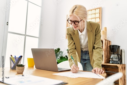 Young blonde woman business worker using laptop writing on document at office