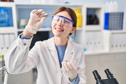 Young blonde woman scientist holding sample with tweezers at laboratory