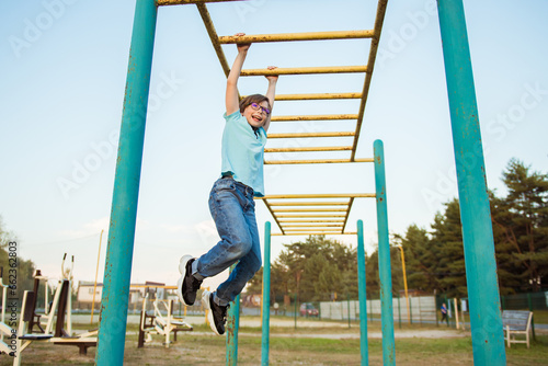 Front view of caucasian sports boy doing hanging hand walk exercise on horizontal bar on sports ground. Modern healthy and sports lifestyle. Daytime © irena_geo