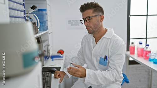 Attractive young hispanic man, working tirelessly in the lab, engrossed scientist holding a test tube, fixated on computer screens while experimenting with cutting-edge medical technology.