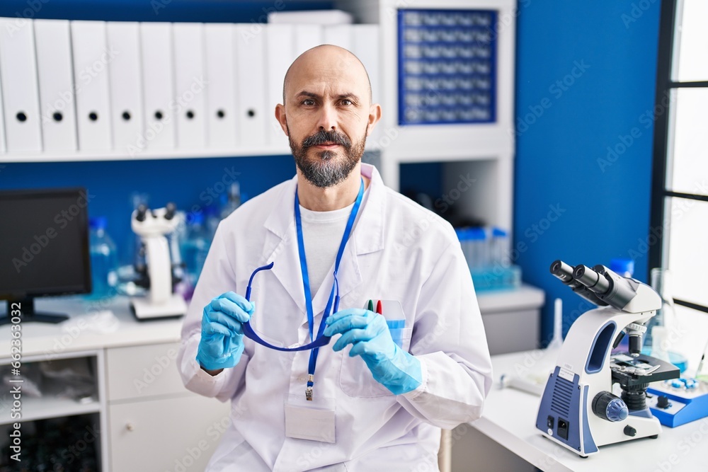 Young bald man scientist holding security glasses at laboratory Young bald man scientist holding security glasses at laboratory