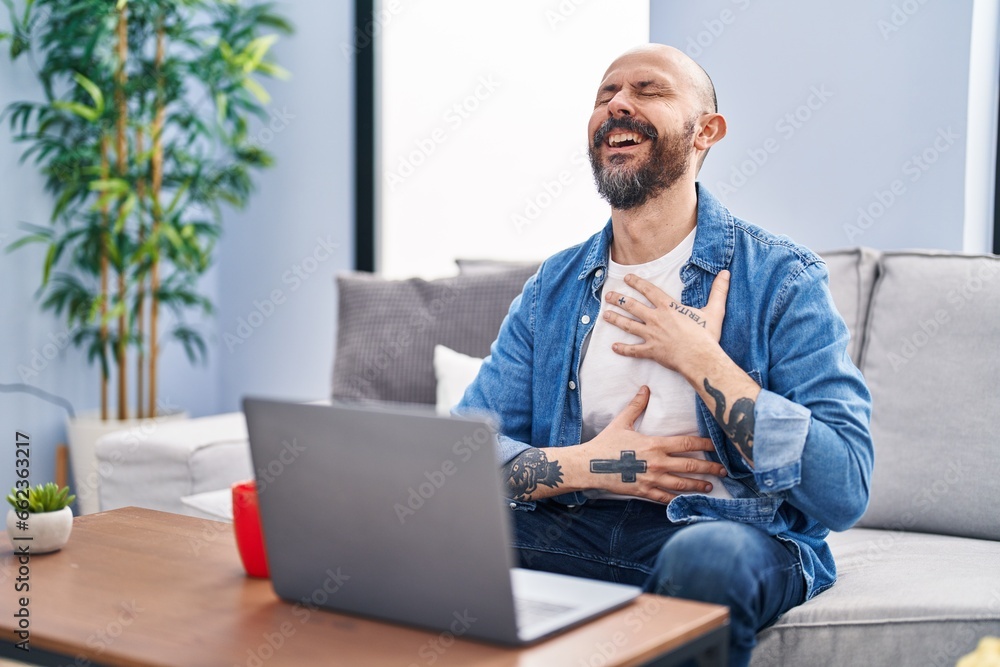 Young bald man having video call sitting on sofa at home