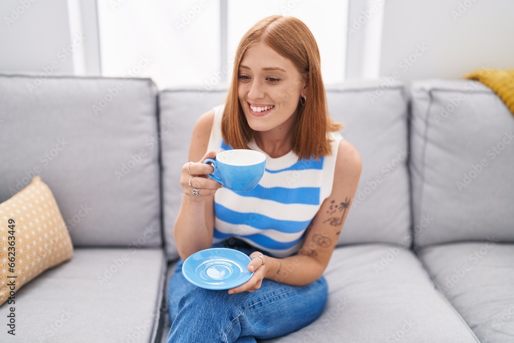 Young redhead woman drinking coffee sitting on sofa at home Young redhead woman drinking coffee sitting on sofa at home