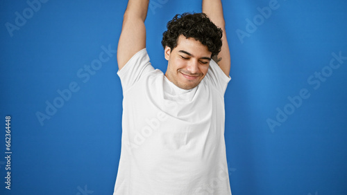 Young latin man stretching arms over isolated blue background photo