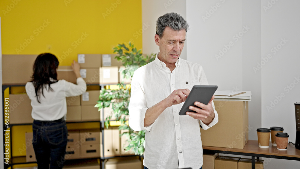 Senior man and woman ecommerce business workers using touchpad working at office