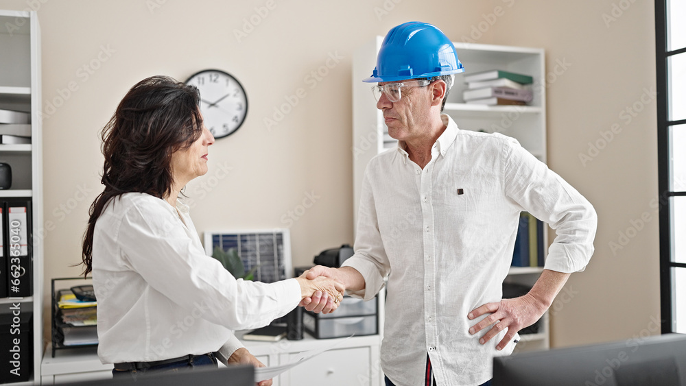 Senior man and woman business worker and architect reading document shake hands at office Senior man and woman business worker and architect reading document shake hands at office