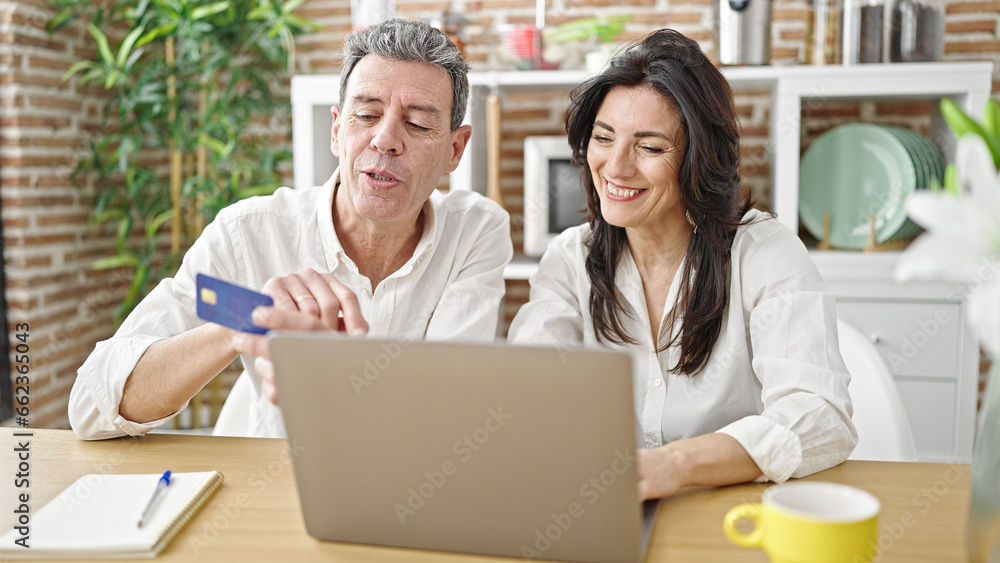 Senior man and woman couple shopping with laptop and credit card at dinning room Senior man and woman couple shopping with laptop and credit card at dinning room