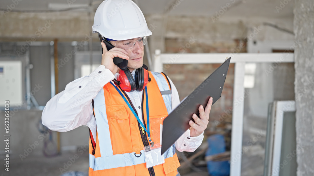 Young caucasian man architect talking on smartphone reading document at construction site Young caucasian man architect talking on smartphone reading document at construction site
