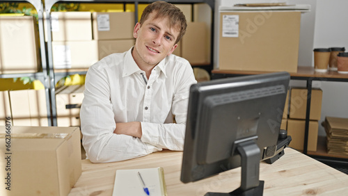 Young caucasian man ecommerce business worker smiling confident sitting with arms crossed gesture at office