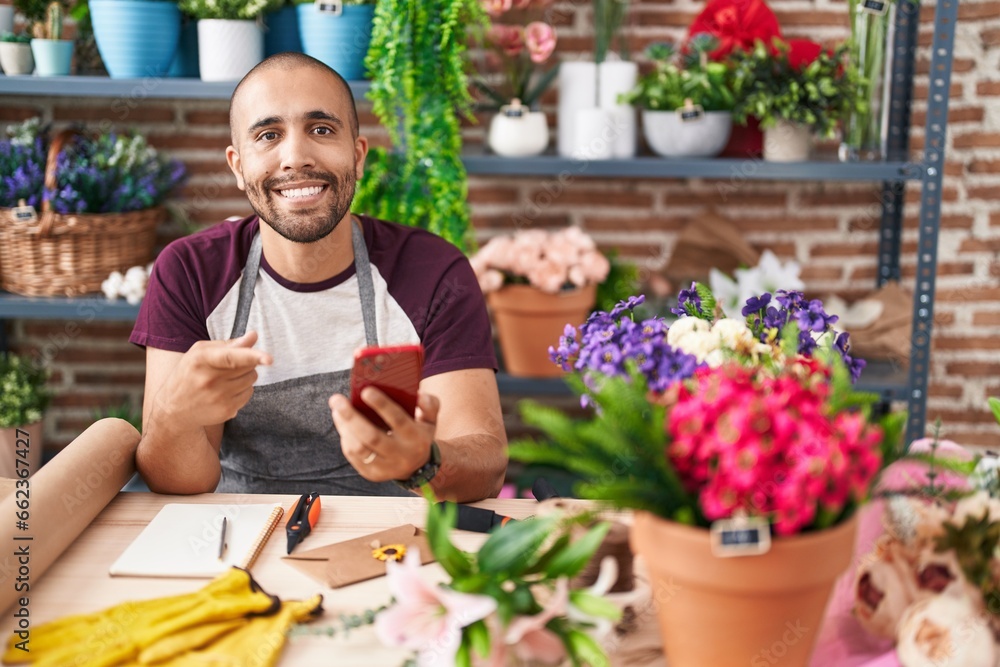 Hispanic man with beard working at florist shop with smartphone smiling happy pointing with hand and finger