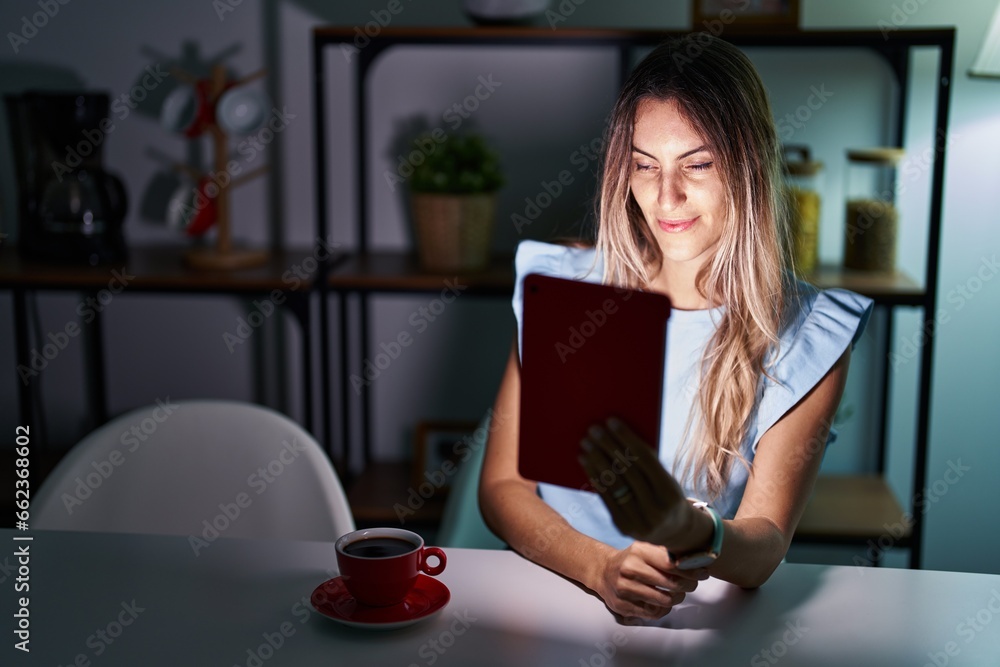 Young hispanic woman using touchpad sitting on the table at night relaxed with serious expression on face. simple and natural looking at the camera. Young hispanic woman using touchpad sitting on the table at night relaxed with serious expression on face. simple and natural looking at the camera.
