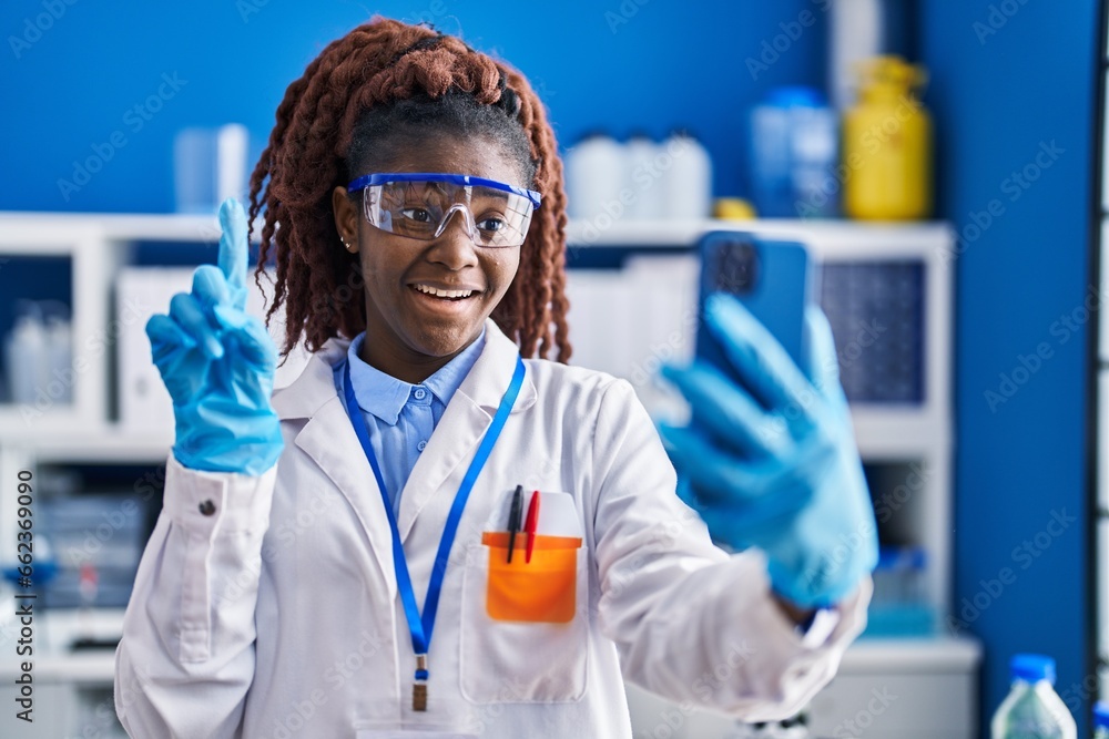 African woman working at scientist laboratory doing video call smiling with an idea or question pointing finger with happy face, number one African woman working at scientist laboratory doing video call smiling with an idea or question pointing finger with happy face, number one