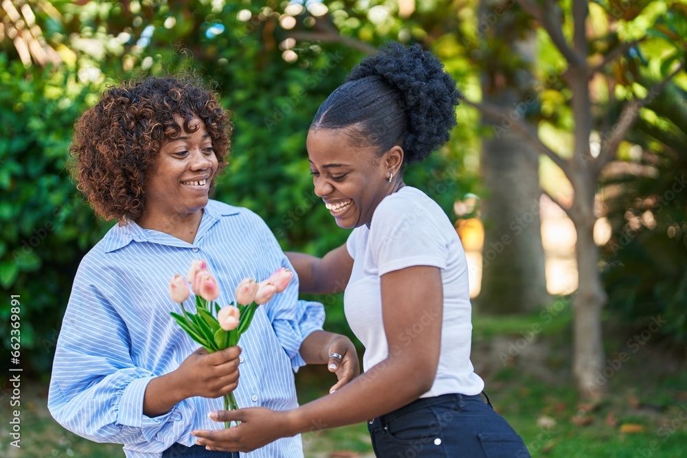 African american women mother and daughter surprise with bouquet of flowers at park African american women mother and daughter surprise with bouquet of flowers at park