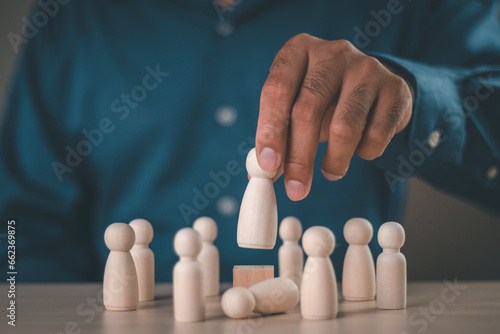 Businessman hand selects a wooden figures human was chosen leadership of teamwork. Concept of leadership, successful competition winner and Leader with influence and winner among the losers.