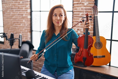 Brunette woman playing violin smiling looking to the side and staring away thinking.
