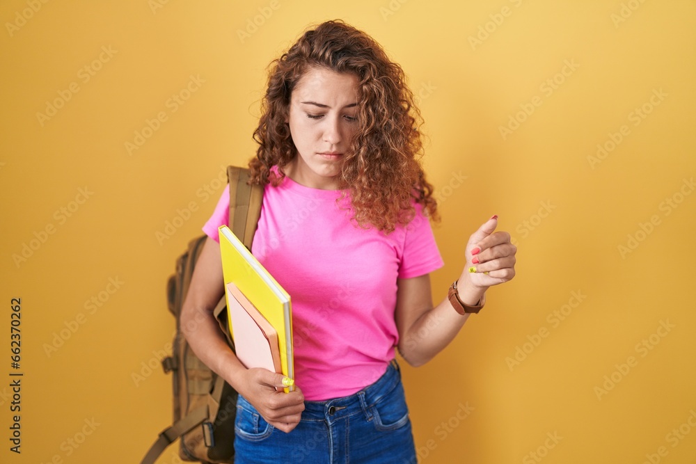 Young caucasian woman wearing student backpack and holding books pointing down looking sad and upset, indicating direction with fingers, unhappy and depressed. Young caucasian woman wearing student backpack and holding books pointing down looking sad and upset, indicating direction with fingers, unhappy and depressed.