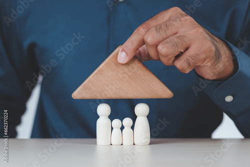 Close-up of a man's hand protecting a wooden family puppet with a wooden block roof. insurance, protection Family Safety, Family Creation, Leadership and Leadership. Wooden figures.