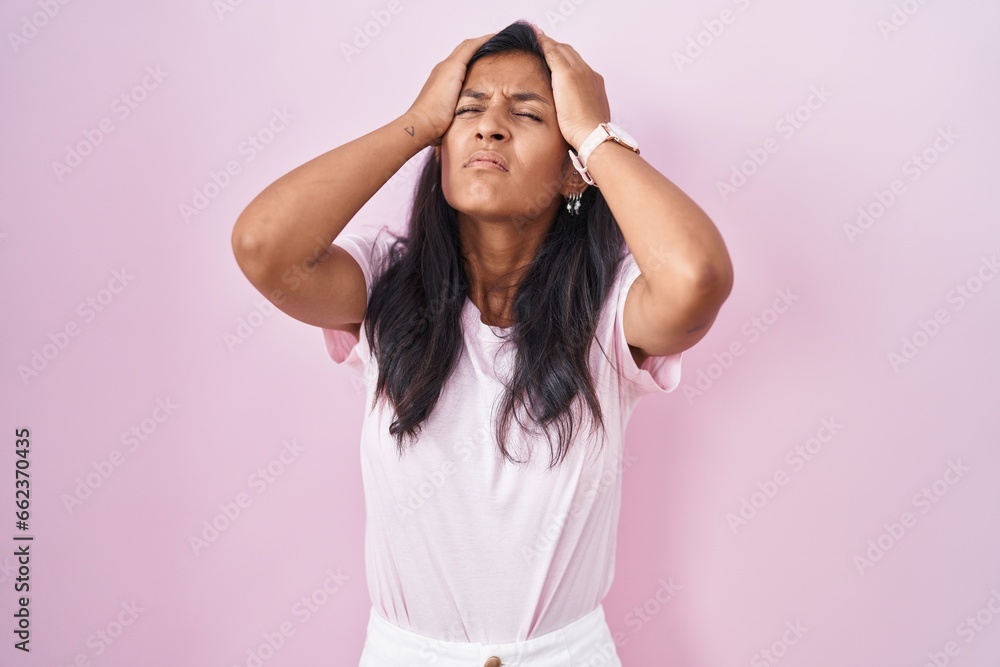 Young hispanic woman standing over pink background suffering from headache desperate and stressed because pain and migraine. hands on head. Young hispanic woman standing over pink background suffering from headache desperate and stressed because pain and migraine. hands on head.