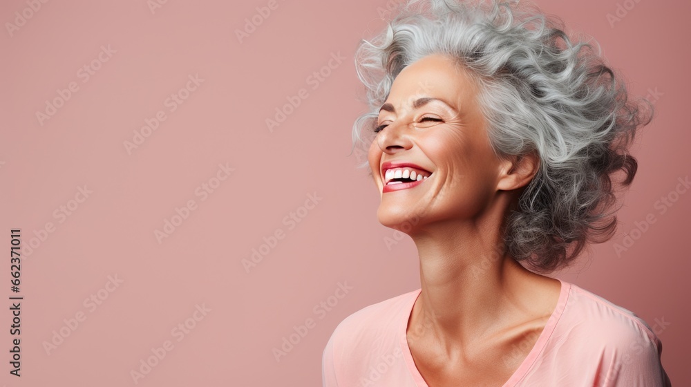 Studio portrait of an elderly woman smiling on a soft pastel background.