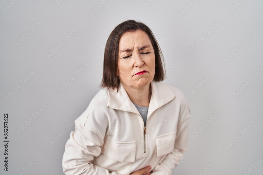 Middle age hispanic woman standing over isolated background with hand on stomach because indigestion, painful illness feeling unwell. ache concept. Middle age hispanic woman standing over isolated background with hand on stomach because indigestion, painful illness feeling unwell. ache concept.