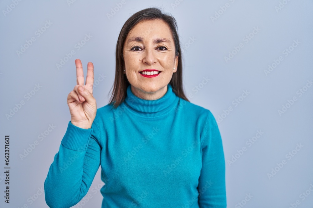 Middle age hispanic woman standing over isolated background showing and pointing up with fingers number two while smiling confident and happy. Middle age hispanic woman standing over isolated background showing and pointing up with fingers number two while smiling confident and happy.