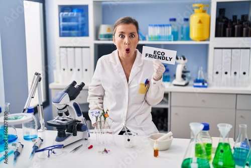 Middle age hispanic woman working at eco friendly laboratory scared and amazed with open mouth for surprise  disbelief face