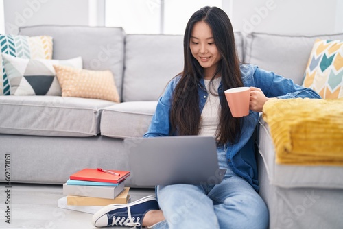 Young chinese woman using laptop drinking coffee at home