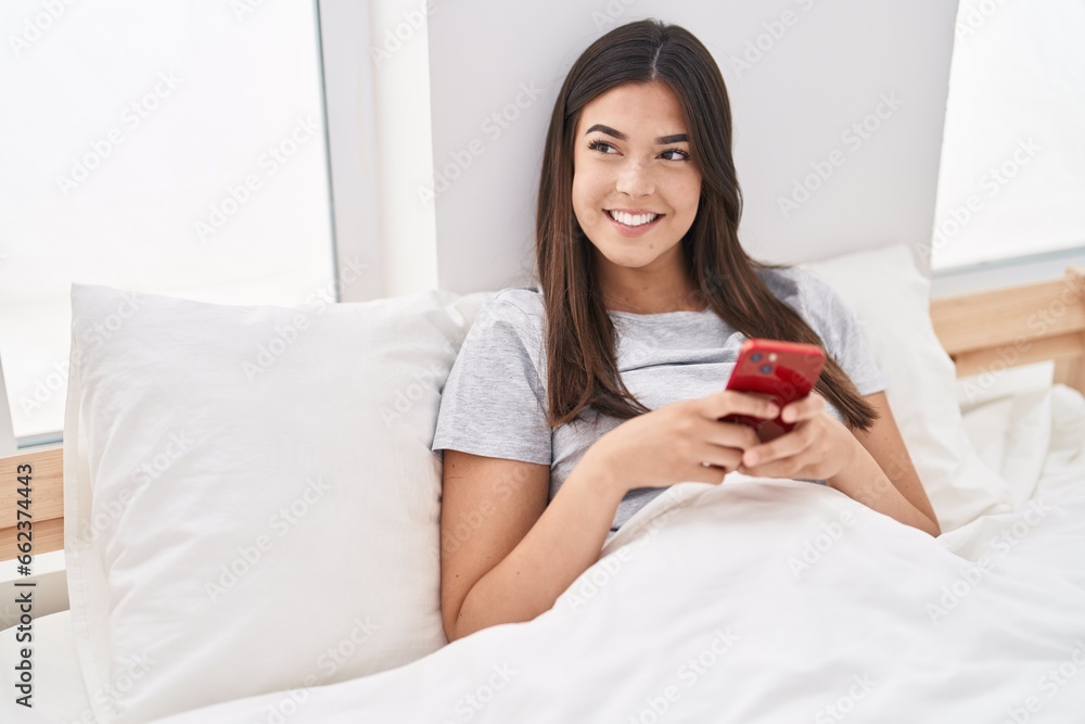 Young beautiful hispanic woman using smartphone sitting on bed at bedroom Young beautiful hispanic woman using smartphone sitting on bed at bedroom
