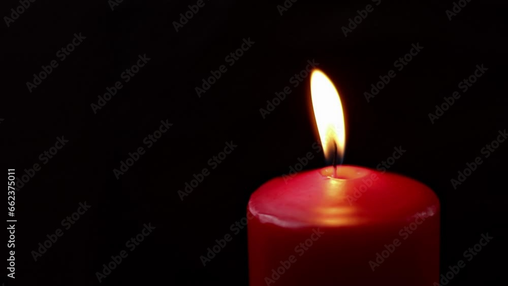 A man extinguishes a burning large festive red candle with his fingers on a solid black background. A man extinguishes a burning large festive red candle with his fingers on a solid black background.