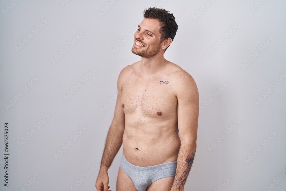 Young hispanic man standing shirtless wearing underware looking away to side with smile on face, natural expression. laughing confident.