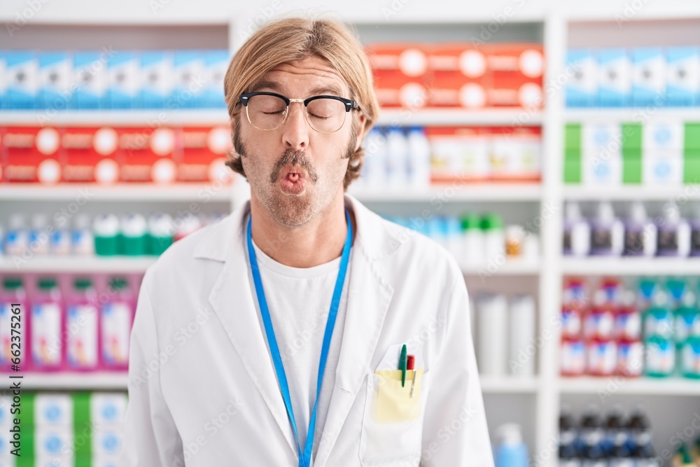 Caucasian man with mustache working at pharmacy drugstore making fish face with lips, crazy and comical gesture. funny expression. Caucasian man with mustache working at pharmacy drugstore making fish face with lips, crazy and comical gesture. funny expression.