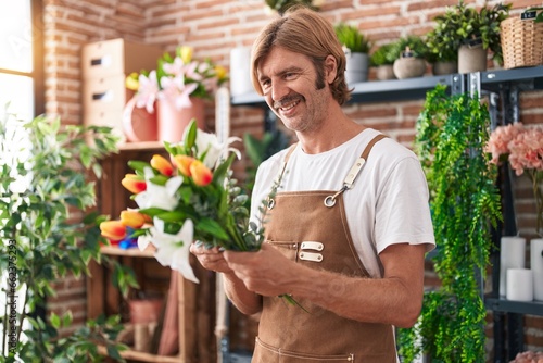 Young blond man florist holding bouquet of flowers at flower shop