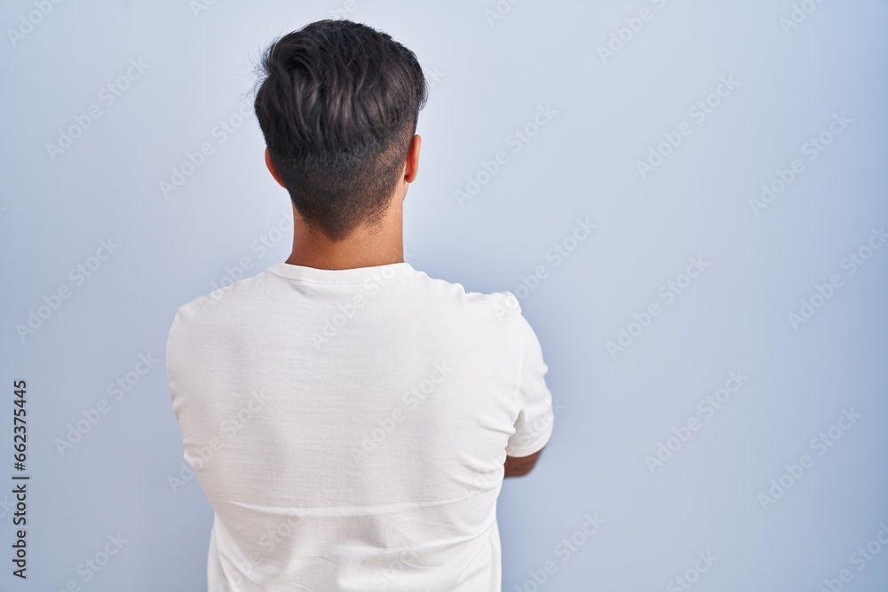 Hispanic man standing over blue background standing backwards looking away with crossed arms Hispanic man standing over blue background standing backwards looking away with crossed arms