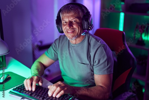Middle age grey-haired man streamer playing video game using computer at gaming room © Krakenimages.com