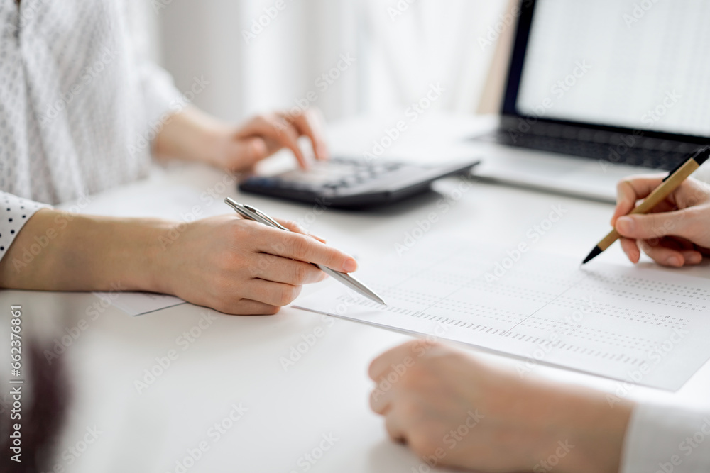 Two accountants using a laptop computer and calculator for counting taxes at white desk in office. Teamwork in business audit and finance Two accountants using a laptop computer and calculator for counting taxes at white desk in office. Teamwork in business audit and finance